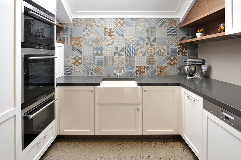 Transitional u-shaped eat-in kitchen in Melbourne with a farmhouse sink, shaker cabinets, white cabinets, quartz benchtops, porcelain splashback, stainless steel appliances, concrete floors and no island.