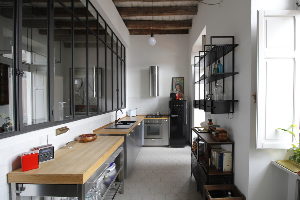 Expansive industrial l-shaped separate kitchen in Turin with a drop-in sink, flat-panel cabinets, stainless steel cabinets, wood benchtops, white splashback, porcelain splashback, stainless steel appliances, cement tiles, grey floor and brown benchtop.