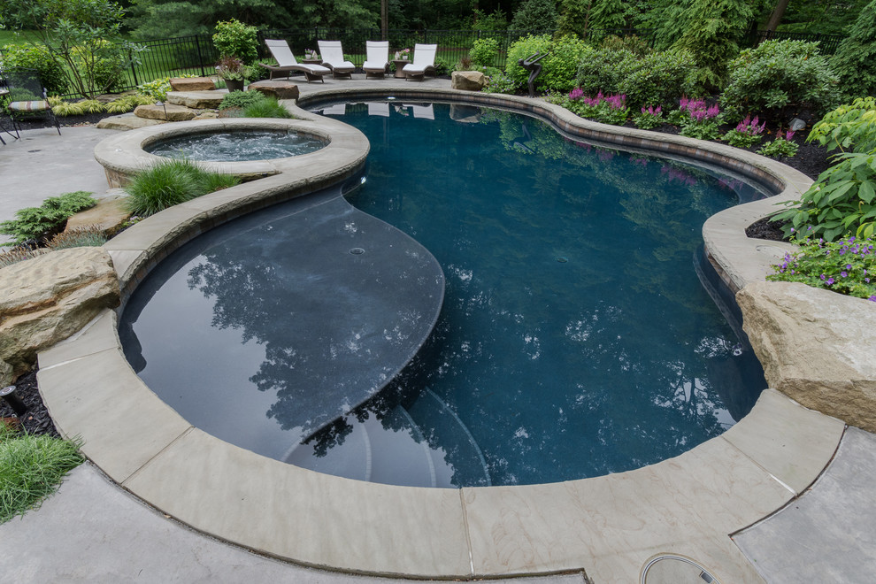 Design ideas for a large traditional backyard custom-shaped pool in Cleveland with a hot tub and concrete pavers.