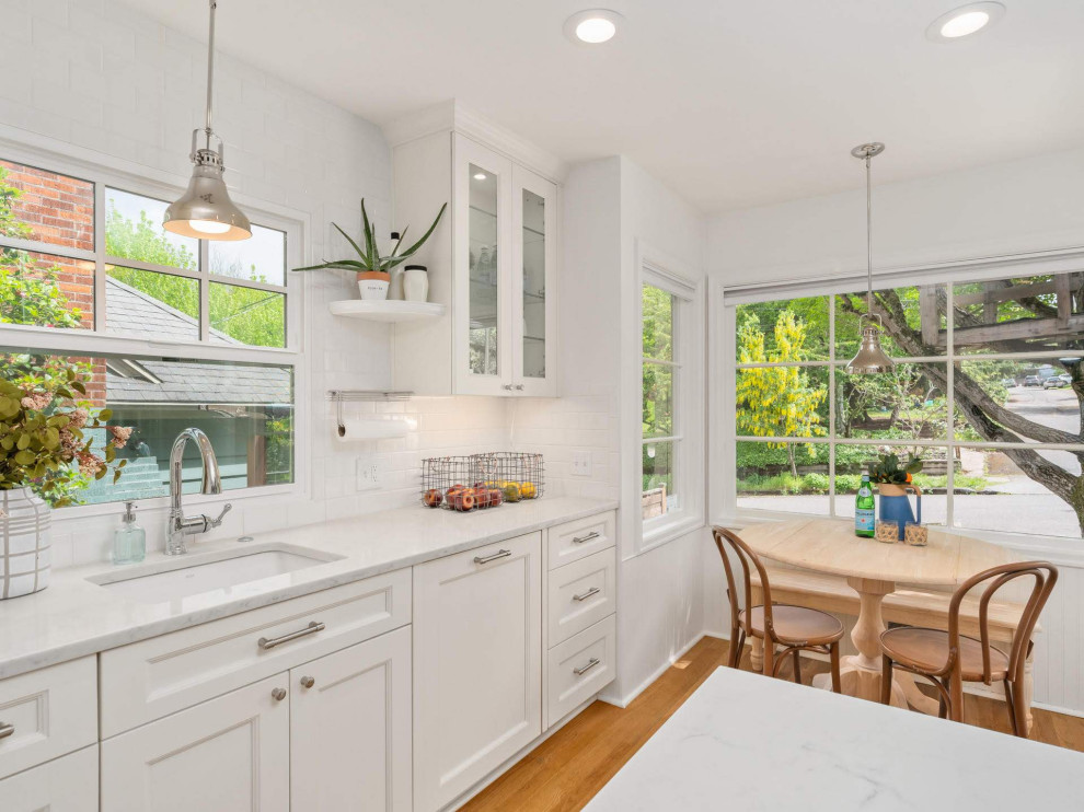 Inspiration for a mid-sized country single-wall eat-in kitchen in Portland with an undermount sink, recessed-panel cabinets, white cabinets, white splashback, panelled appliances, medium hardwood floors, with island, brown floor, white benchtop, quartzite benchtops and ceramic splashback.