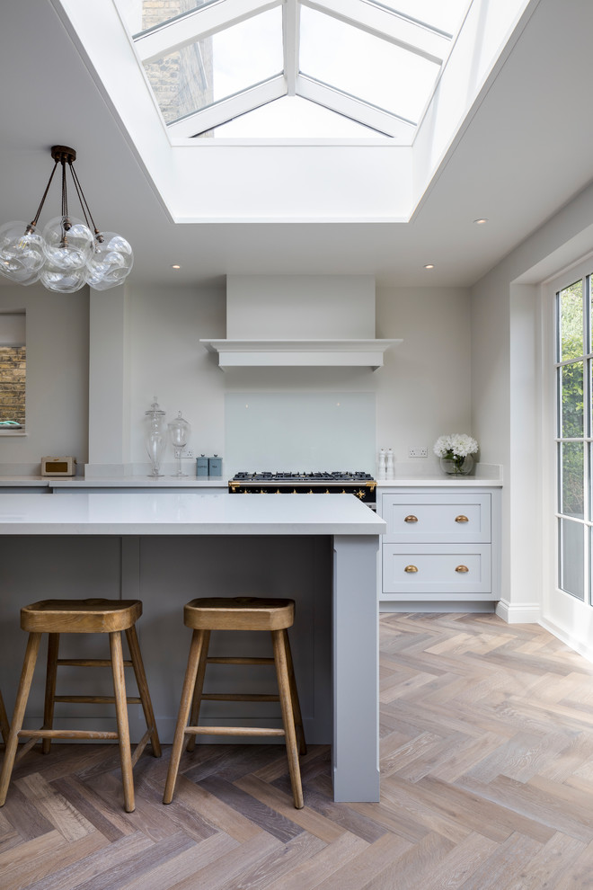 Inspiration for a mid-sized transitional l-shaped eat-in kitchen in London with a farmhouse sink, shaker cabinets, blue cabinets, stainless steel appliances, medium hardwood floors, a peninsula and brown floor.
