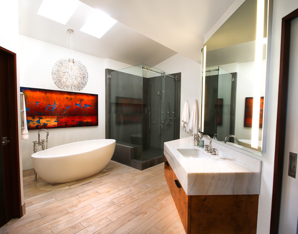 Inspiration for a large contemporary master bathroom in Denver with flat-panel cabinets, light wood cabinets, a freestanding tub, a corner shower, gray tile, porcelain tile, white walls, porcelain floors, an undermount sink, onyx benchtops, beige floor, a sliding shower screen and white benchtops.