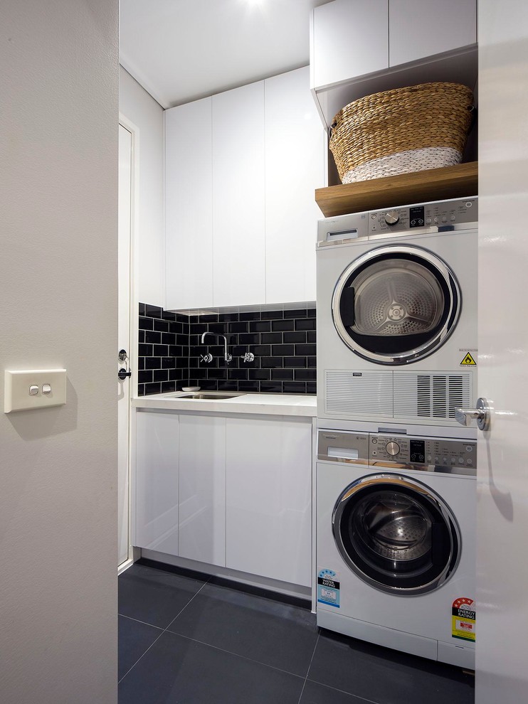 Photo of a small contemporary single-wall dedicated laundry room in Melbourne with white cabinets, granite benchtops, ceramic floors, a stacked washer and dryer, an undermount sink, flat-panel cabinets, grey floor and grey walls.