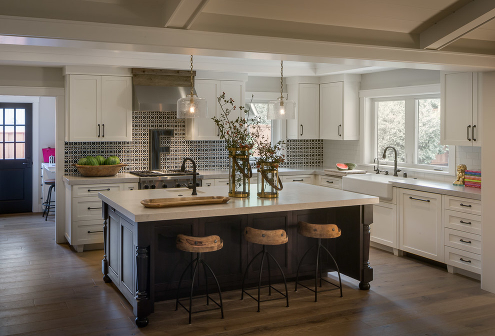 Mid-sized transitional l-shaped kitchen in San Francisco with a farmhouse sink, shaker cabinets, white cabinets, white splashback, subway tile splashback, stainless steel appliances, dark hardwood floors, with island, marble benchtops and brown floor.