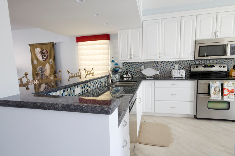 Design ideas for a small beach style l-shaped open plan kitchen in Miami with an undermount sink, raised-panel cabinets, white cabinets, granite benchtops, multi-coloured splashback, glass tile splashback, stainless steel appliances, ceramic floors and a peninsula.