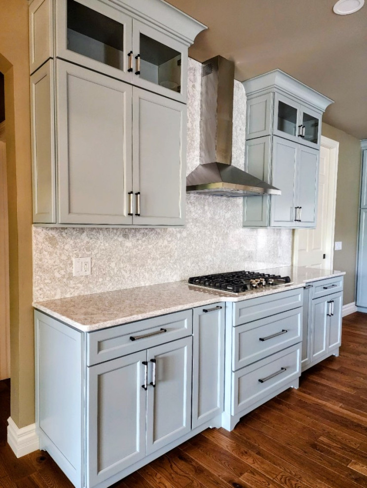 Example of a mid-sized transitional medium tone wood floor and brown floor open concept kitchen design with an undermount sink, shaker cabinets, quartz countertops, white backsplash, quartz backsplash, stainless steel appliances, an island and white countertops