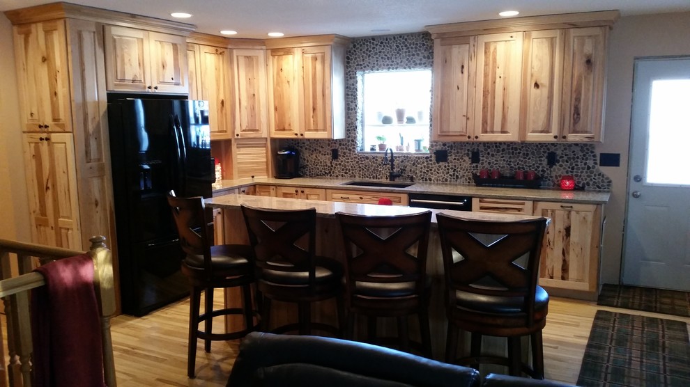 Mid-sized mountain style l-shaped medium tone wood floor and brown floor open concept kitchen photo with a double-bowl sink, raised-panel cabinets, light wood cabinets, granite countertops, multicolored backsplash, stone tile backsplash, black appliances and an island