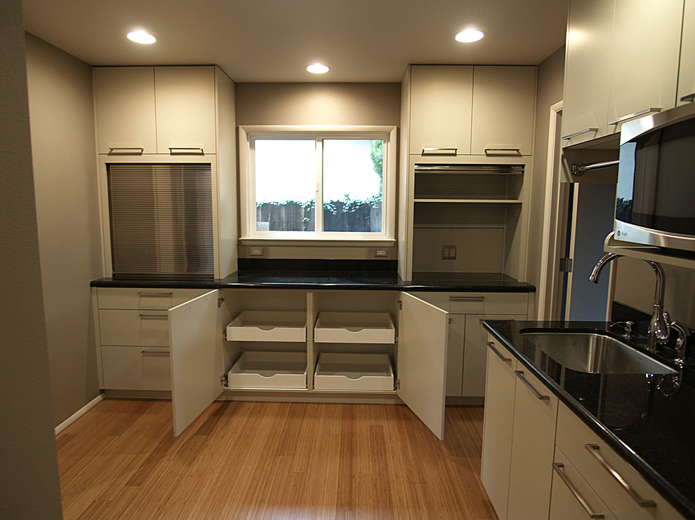 Small modern l-shaped kitchen pantry in Sacramento with an undermount sink, flat-panel cabinets, beige cabinets, granite benchtops, beige splashback, glass tile splashback, stainless steel appliances, bamboo floors and no island.