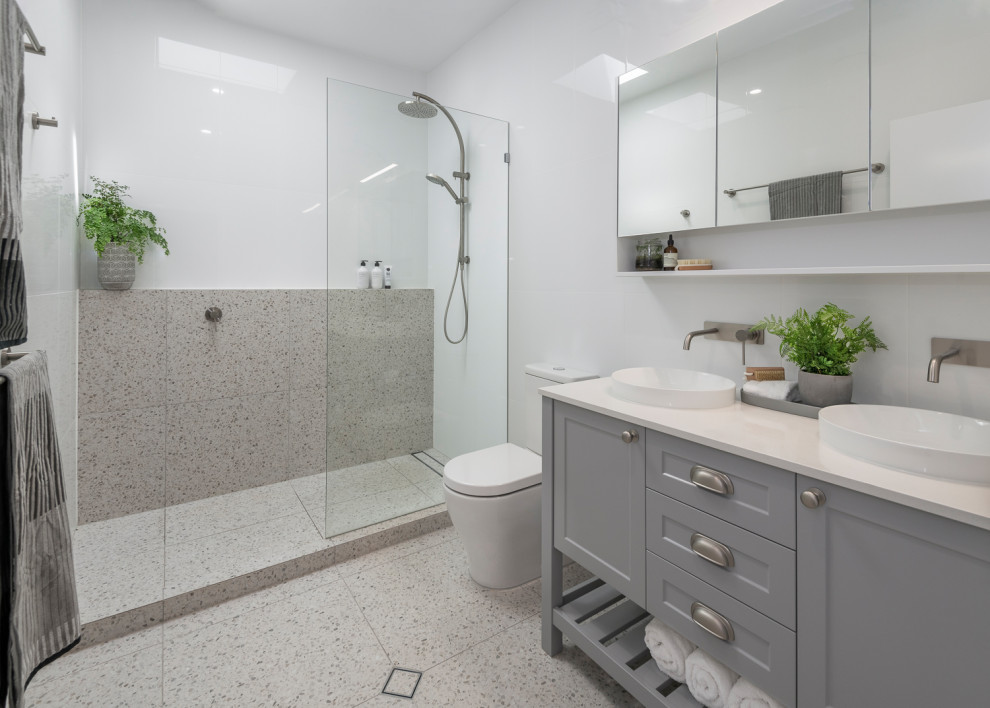 Inspiration for a mid-sized transitional 3/4 bathroom in Brisbane with shaker cabinets, grey cabinets, an open shower, a one-piece toilet, white tile, porcelain tile, white walls, terrazzo floors, a vessel sink, solid surface benchtops, grey floor, an open shower and white benchtops.