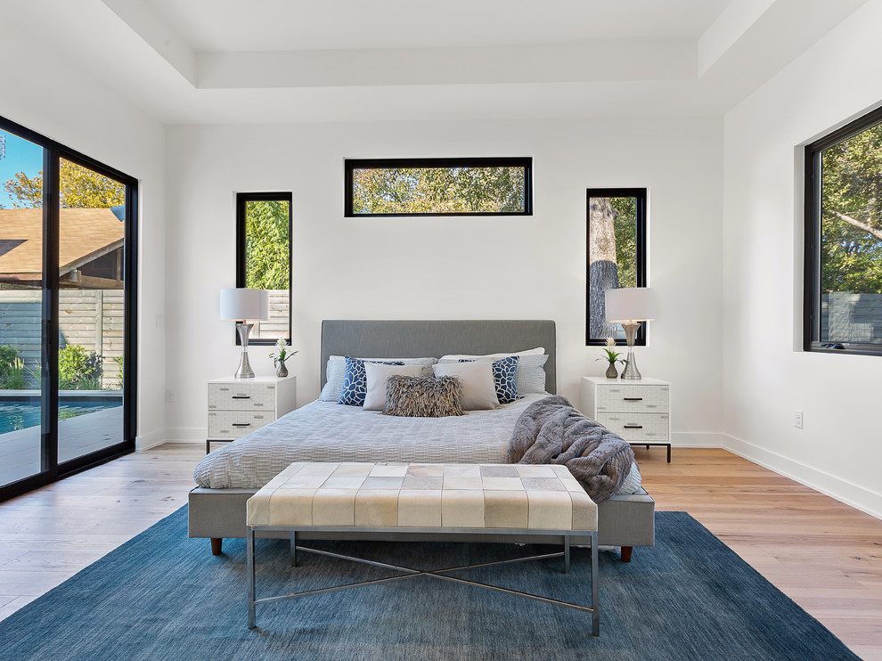 This is an example of a large contemporary master bedroom in Austin with white walls, light hardwood floors and no fireplace.