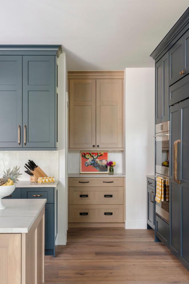 Inredning av ett klassiskt mellanstort vit vitt kök, med en undermonterad diskho, skåp i shakerstil, blå skåp, bänkskiva i kvartsit, vitt stänkskydd, stänkskydd i keramik, integrerade vitvaror, mellanmörkt trägolv, en köksö och beiget golv
