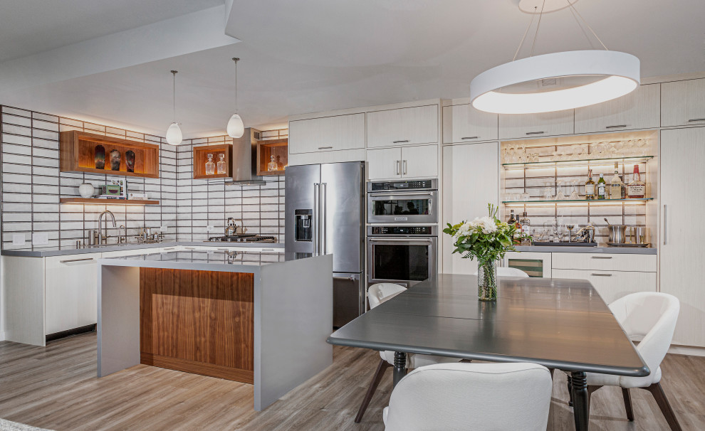 This is an example of a mid-sized contemporary l-shaped open plan kitchen in San Diego with an undermount sink, flat-panel cabinets, white cabinets, glass benchtops, multi-coloured splashback, ceramic splashback, stainless steel appliances, vinyl floors, with island, brown floor and grey benchtop.