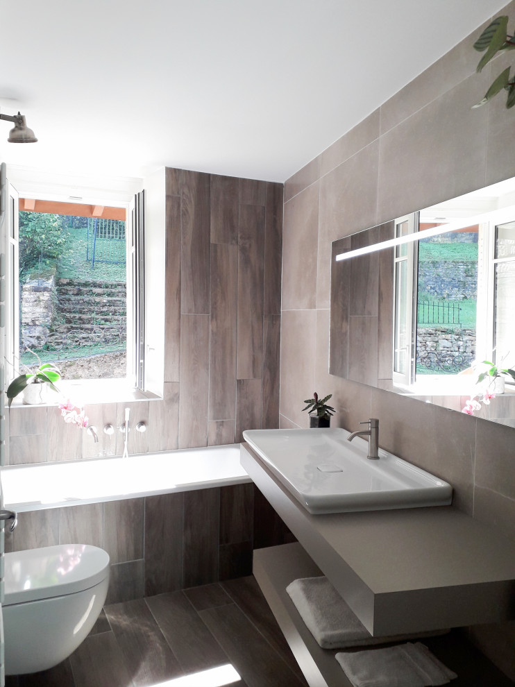 Inspiration för små moderna brunt badrum för barn, med luckor med profilerade fronter, bruna skåp, ett undermonterat badkar, en vägghängd toalettstol, brun kakel, ett avlångt handfat, laminatbänkskiva och brunt golv