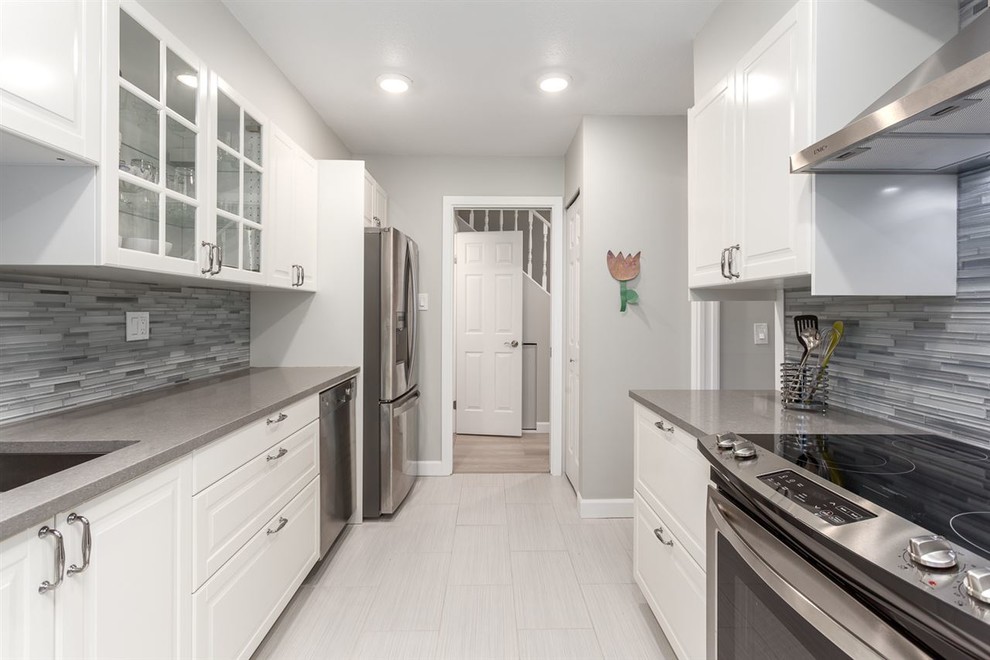 Design ideas for a mid-sized contemporary galley separate kitchen in Vancouver with an undermount sink, raised-panel cabinets, white cabinets, solid surface benchtops, grey splashback, glass tile splashback, stainless steel appliances, ceramic floors, no island and white floor.