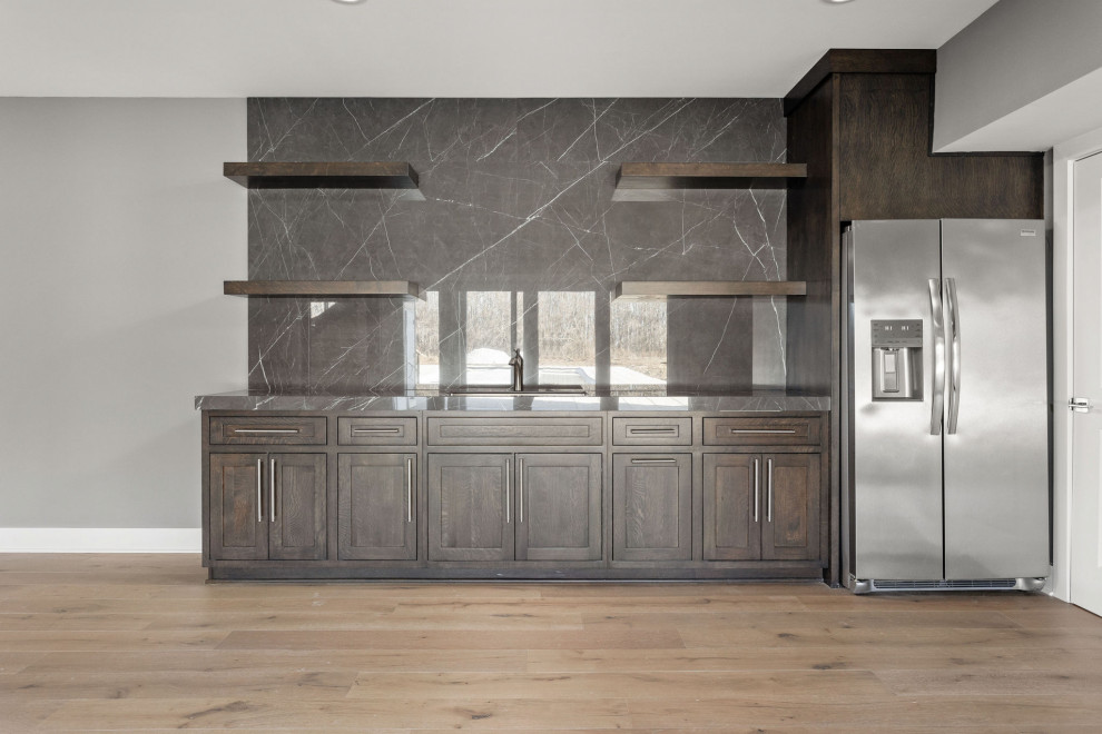 Inspiration for a large modern galley home bar in Indianapolis with an undermount sink, shaker cabinets, dark wood cabinets, grey splashback, light hardwood floors, multi-coloured floor and grey benchtop.