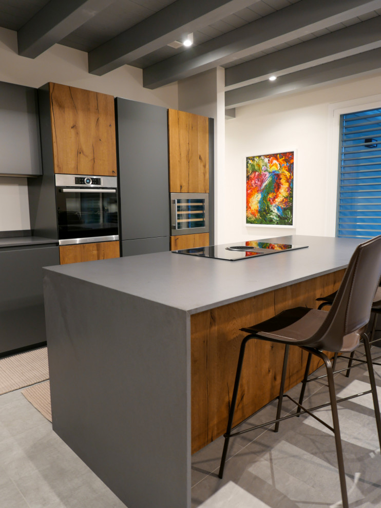 Large modern l-shaped open plan kitchen in Other with an undermount sink, flat-panel cabinets, medium wood cabinets, laminate benchtops, grey splashback, stainless steel appliances, porcelain floors, with island, grey floor, grey benchtop and exposed beam.