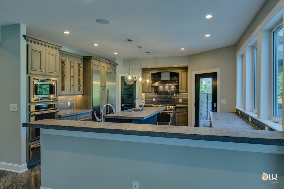 Enclosed kitchen - transitional l-shaped medium tone wood floor and brown floor enclosed kitchen idea with an undermount sink, raised-panel cabinets, distressed cabinets, soapstone countertops, gray backsplash, subway tile backsplash, stainless steel appliances and an island