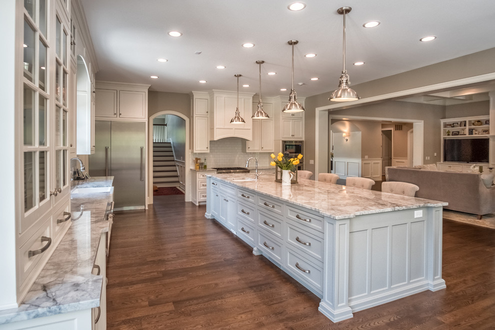 Inspiration for a large transitional l-shaped eat-in kitchen in Other with a farmhouse sink, shaker cabinets, white cabinets, marble benchtops, white splashback, subway tile splashback, stainless steel appliances, medium hardwood floors and with island.
