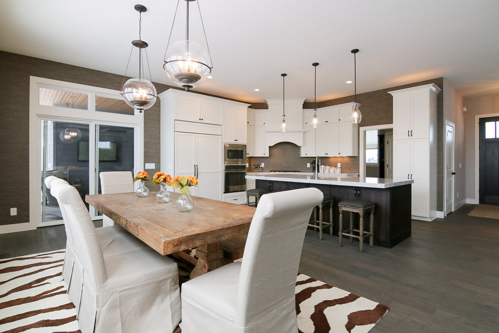 Example of a large transitional u-shaped medium tone wood floor and brown floor eat-in kitchen design with a drop-in sink, recessed-panel cabinets, white cabinets, marble countertops, beige backsplash, stone tile backsplash, stainless steel appliances and an island