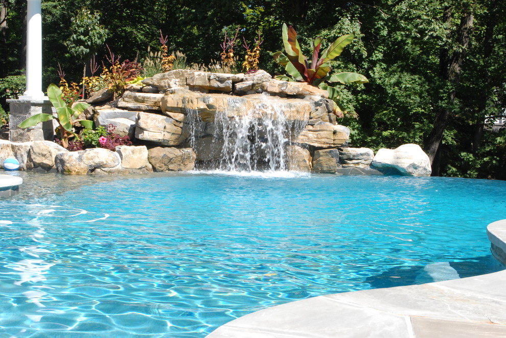 Design ideas for a large tropical backyard custom-shaped infinity pool in New York with a water feature and natural stone pavers.