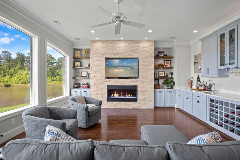 Photo of a large beach style open concept family room in Raleigh with a home bar, white walls, dark hardwood floors, a standard fireplace, a wall-mounted tv and brown floor.