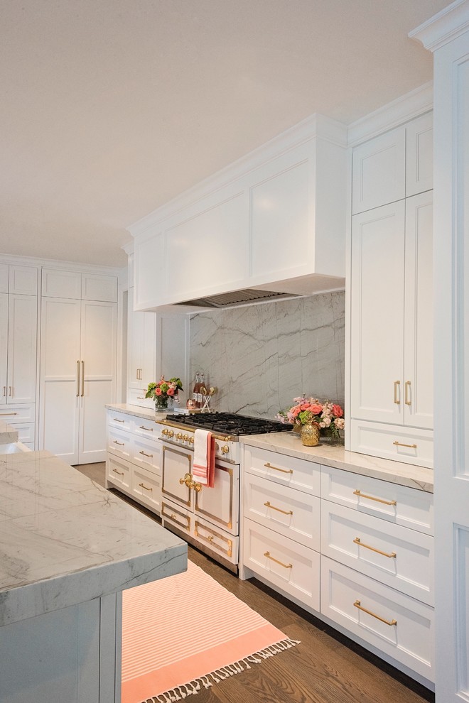 Inspiration for a large transitional l-shaped medium tone wood floor and brown floor open concept kitchen remodel with a farmhouse sink, recessed-panel cabinets, white cabinets, quartzite countertops, white backsplash, stone slab backsplash, paneled appliances and an island