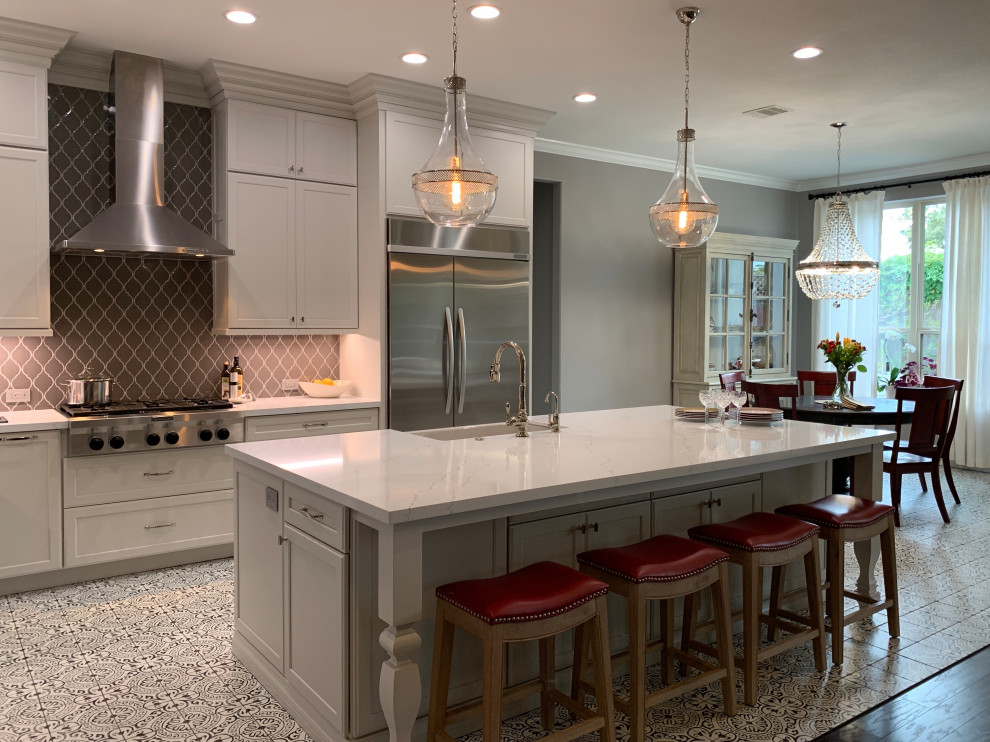 Example of a transitional l-shaped porcelain tile and multicolored floor kitchen design in Houston with a farmhouse sink, recessed-panel cabinets, white cabinets, quartz countertops, gray backsplash, ceramic backsplash, stainless steel appliances, an island and white countertops