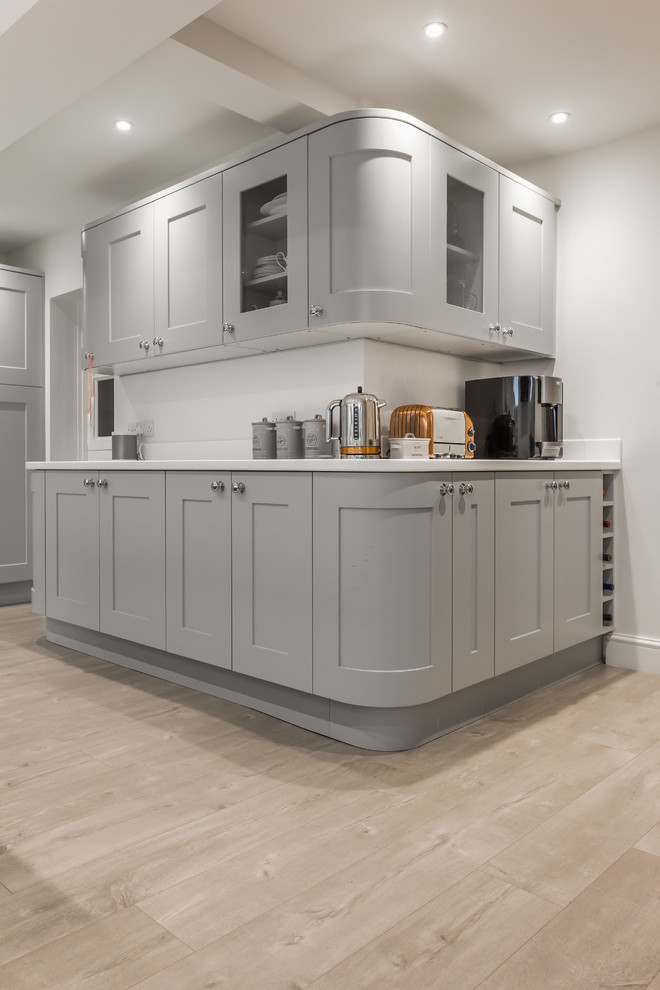 Design ideas for a large transitional l-shaped open plan kitchen in Dorset with a drop-in sink, recessed-panel cabinets, grey cabinets, stainless steel appliances, light hardwood floors and with island.