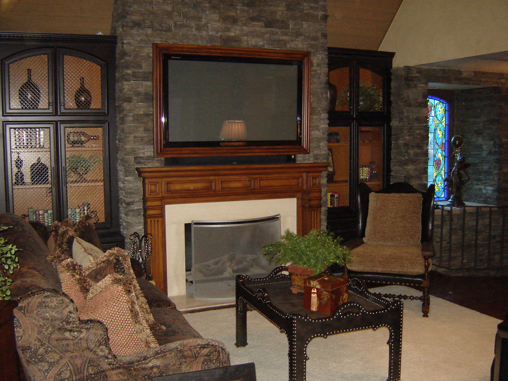 Photo of a mid-sized mediterranean open concept family room in San Luis Obispo with a library, beige walls, carpet, a standard fireplace, a stone fireplace surround and a built-in media wall.