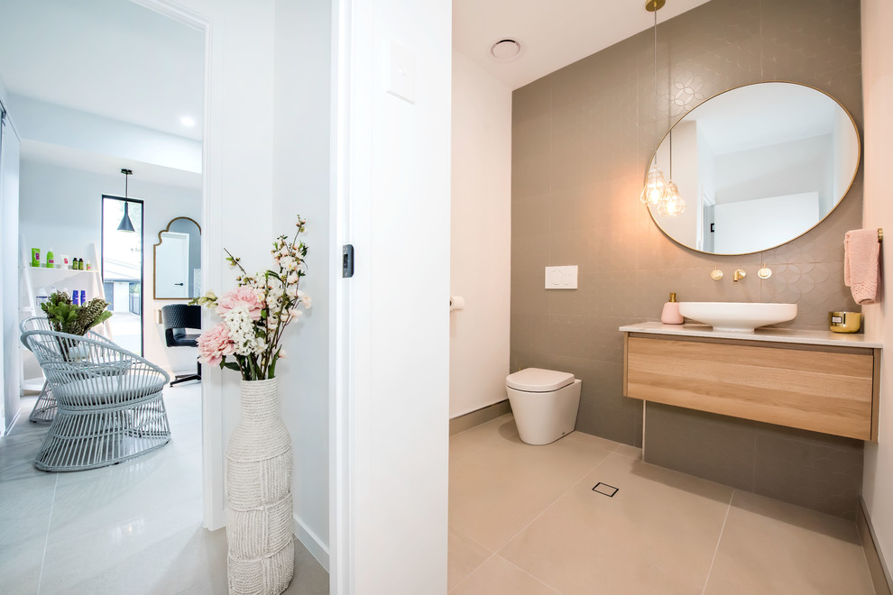 This is an example of a mid-sized contemporary bathroom in Other with flat-panel cabinets, light wood cabinets, a wall-mount toilet, brown tile, ceramic tile, white walls, ceramic floors, a vessel sink, granite benchtops, white floor, white benchtops, a single vanity and a floating vanity.