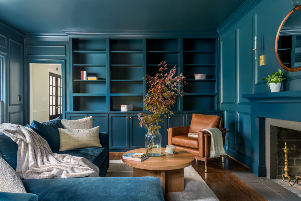 Cette image montre une salle de séjour traditionnelle de taille moyenne avec une bibliothèque ou un coin lecture, un mur bleu, parquet foncé, une cheminée standard, un manteau de cheminée en brique, un sol marron et du lambris.