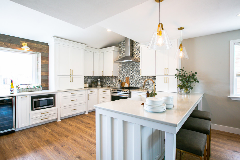 Mid-sized transitional u-shaped eat-in kitchen in Denver with a farmhouse sink, shaker cabinets, white cabinets, quartz benchtops, multi-coloured splashback, cement tile splashback, stainless steel appliances, vinyl floors, a peninsula, brown floor and grey benchtop.