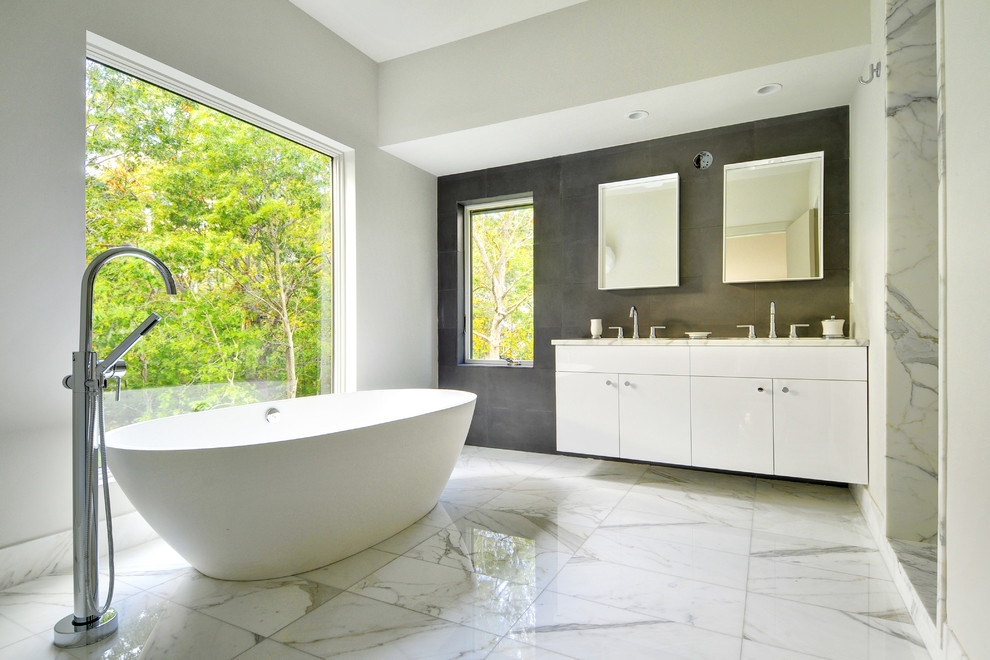 Large trendy master white tile and stone tile marble floor and gray floor freestanding bathtub photo in Boston with marble countertops, flat-panel cabinets, white cabinets, white walls and an undermount sink