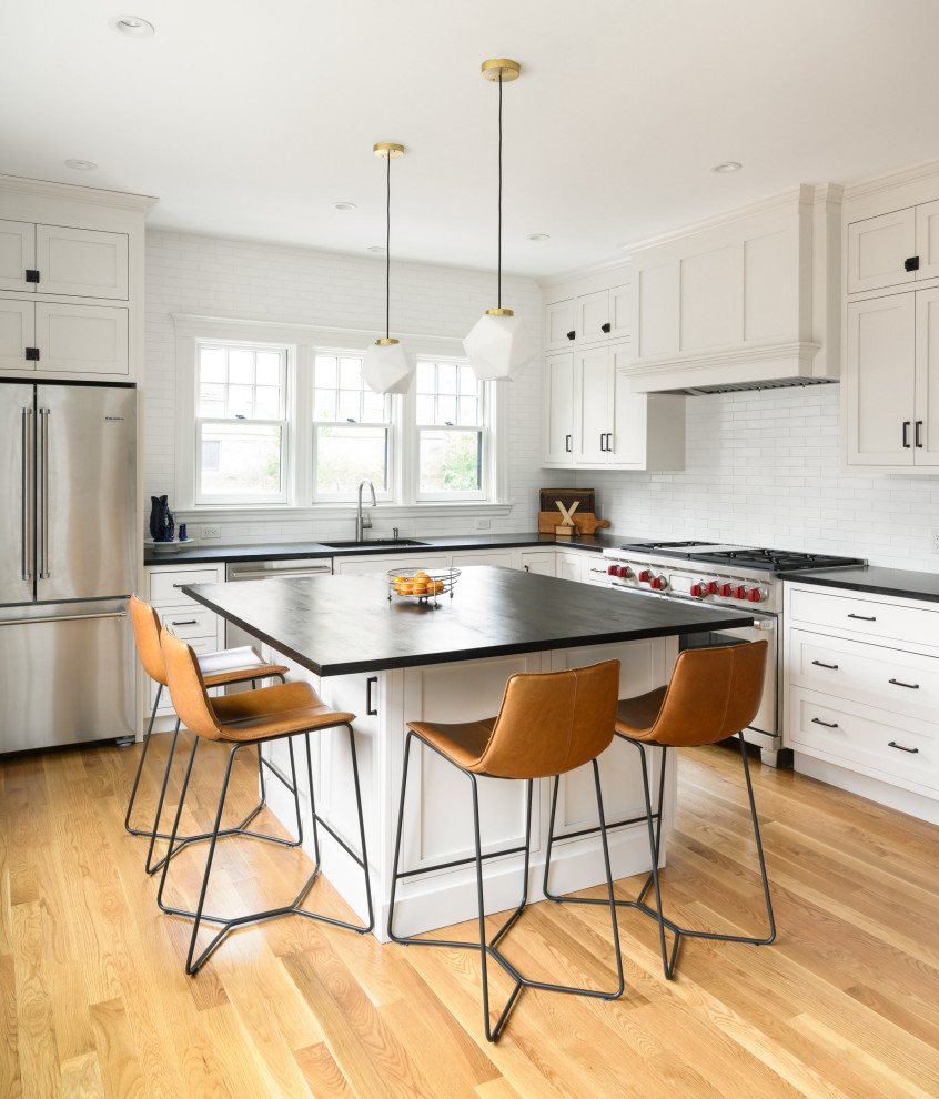 Inspiration for a transitional l-shaped kitchen in Boston with shaker cabinets, white cabinets, soapstone benchtops, white splashback, subway tile splashback, stainless steel appliances, light hardwood floors, with island, black benchtop and a single-bowl sink.