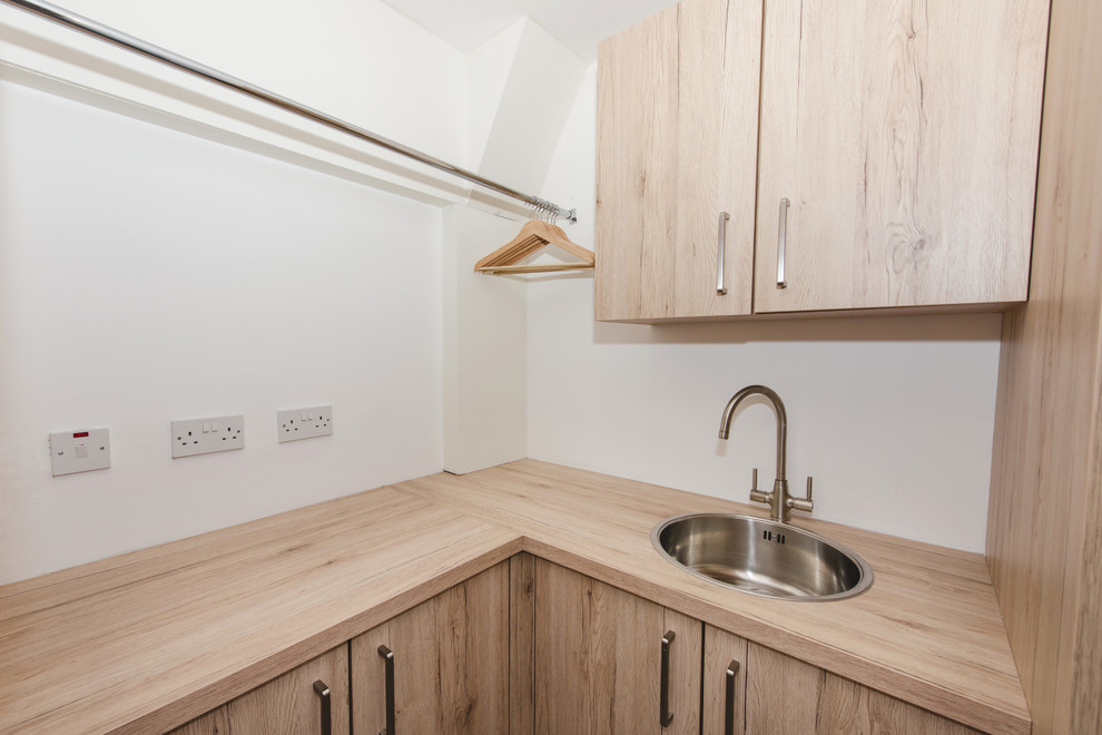 Photo of a modern laundry room in Other with flat-panel cabinets, laminate benchtops, timber splashback, light hardwood floors and light wood cabinets.