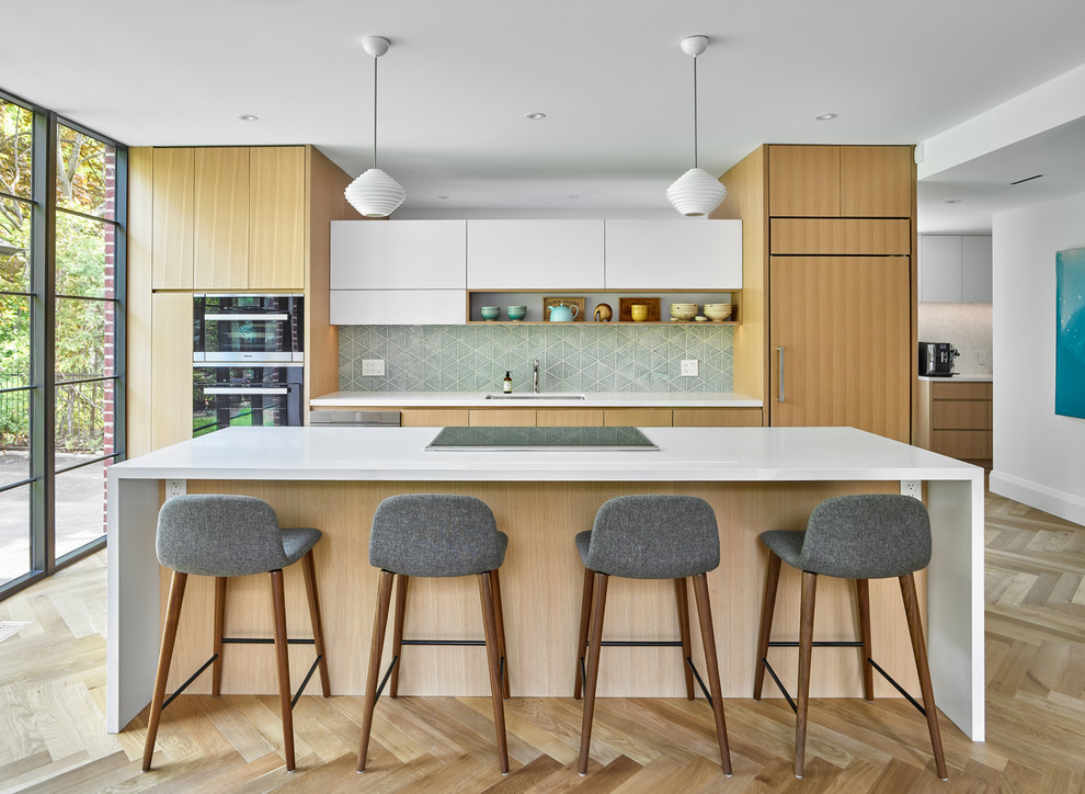 Design ideas for a large contemporary single-wall eat-in kitchen in Toronto with an integrated sink, flat-panel cabinets, light wood cabinets, quartz benchtops, green splashback, ceramic splashback, black appliances, light hardwood floors, with island, brown floor and white benchtop.