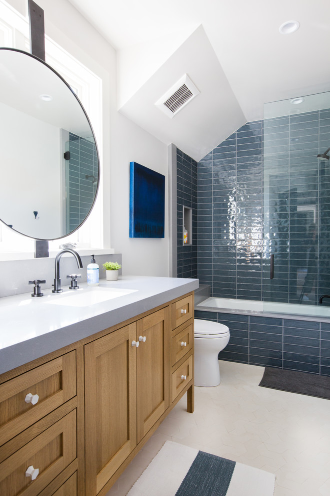 Photo of a beach style bathroom in Orange County with shaker cabinets, medium wood cabinets, an alcove tub, a shower/bathtub combo, blue tile, white walls, mosaic tile floors, an undermount sink, beige floor, an open shower and grey benchtops.
