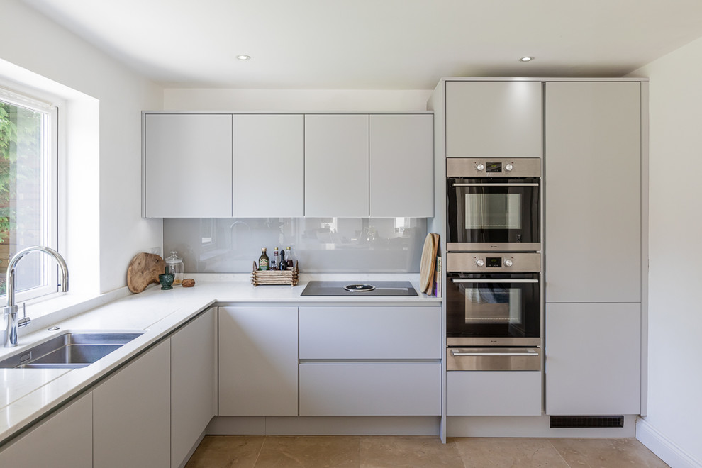 Photo of a contemporary u-shaped eat-in kitchen in Buckinghamshire with a drop-in sink, flat-panel cabinets, grey cabinets, quartzite benchtops, glass sheet splashback, stainless steel appliances and white benchtop.