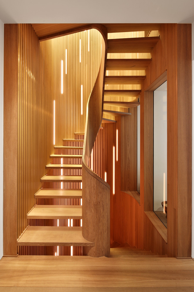 Mid-sized contemporary wood curved staircase in Munich with open risers, wood railing and wood walls.
