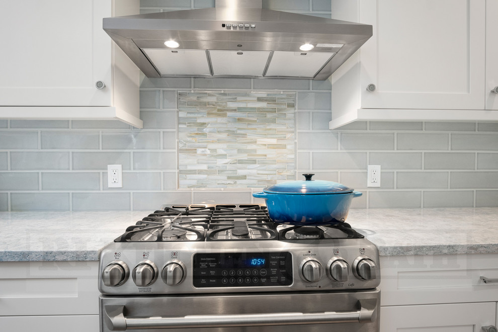 Example of a mid-sized beach style u-shaped medium tone wood floor and brown floor eat-in kitchen design in Providence with a double-bowl sink, shaker cabinets, white cabinets, quartz countertops, blue backsplash, porcelain backsplash, stainless steel appliances, an island and multicolored countertops