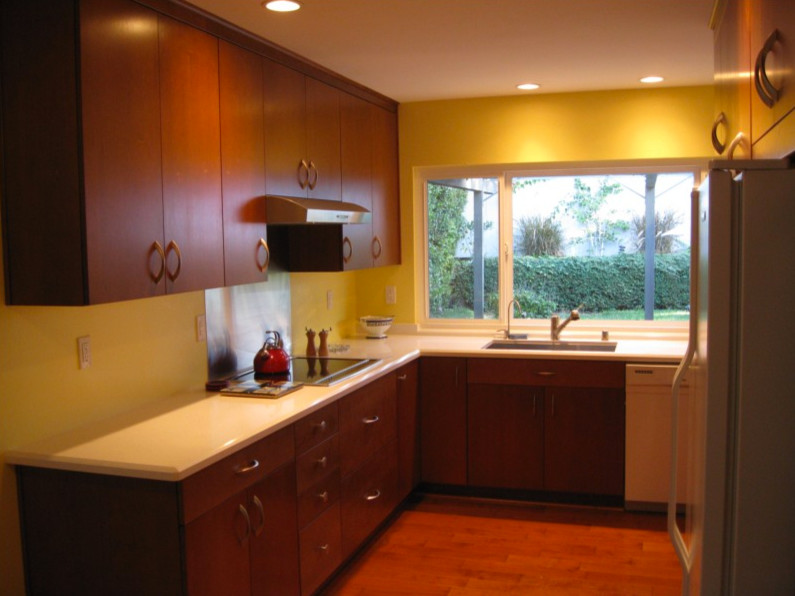 Photo of a small contemporary u-shaped separate kitchen in San Diego with an undermount sink, flat-panel cabinets, medium wood cabinets, solid surface benchtops, white appliances, medium hardwood floors, no island and red floor.