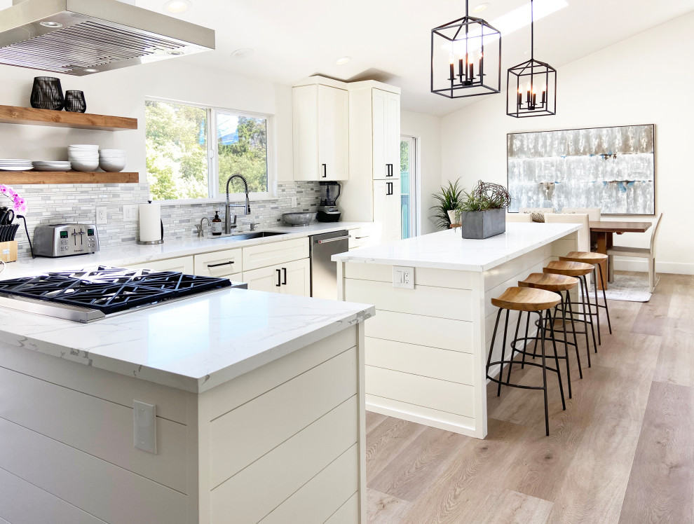 Inspiration for a mid-sized transitional l-shaped vinyl floor, brown floor and vaulted ceiling eat-in kitchen remodel with an undermount sink, shaker cabinets, white cabinets, quartz countertops, multicolored backsplash, mosaic tile backsplash, stainless steel appliances, an island and white countertops