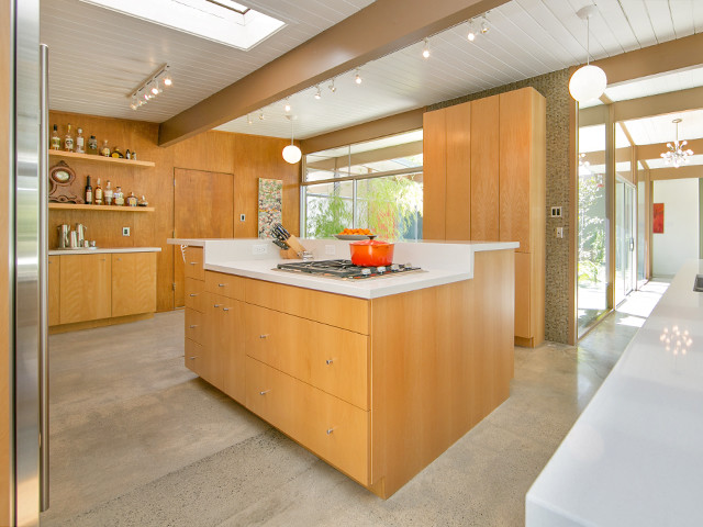 Cette photo montre une grande cuisine américaine rétro en bois clair avec un placard à porte plane, un électroménager en acier inoxydable, un sol en travertin et îlot.
