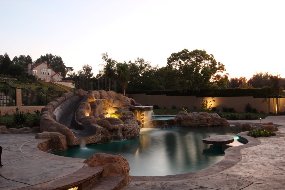 Design ideas for a large traditional backyard custom-shaped pool in Los Angeles with a water slide and stamped concrete.