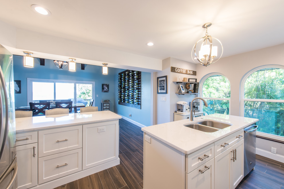 Large transitional u-shaped porcelain tile and brown floor eat-in kitchen photo with an undermount sink, shaker cabinets, white cabinets, quartz countertops, white backsplash, marble backsplash, stainless steel appliances and two islands