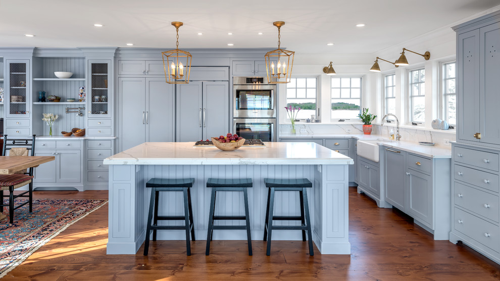 Inspiration for a beach style l-shaped eat-in kitchen in Portland Maine with a farmhouse sink, shaker cabinets, blue cabinets, white splashback, panelled appliances, medium hardwood floors, with island and white benchtop.