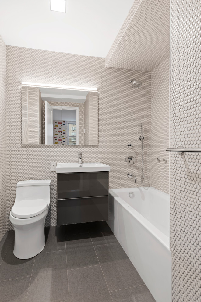 Design ideas for a small contemporary 3/4 bathroom in New York with an alcove tub, porcelain floors, flat-panel cabinets, grey cabinets, an alcove shower, a one-piece toilet, beige tile, mosaic tile, beige walls, a drop-in sink and grey floor.