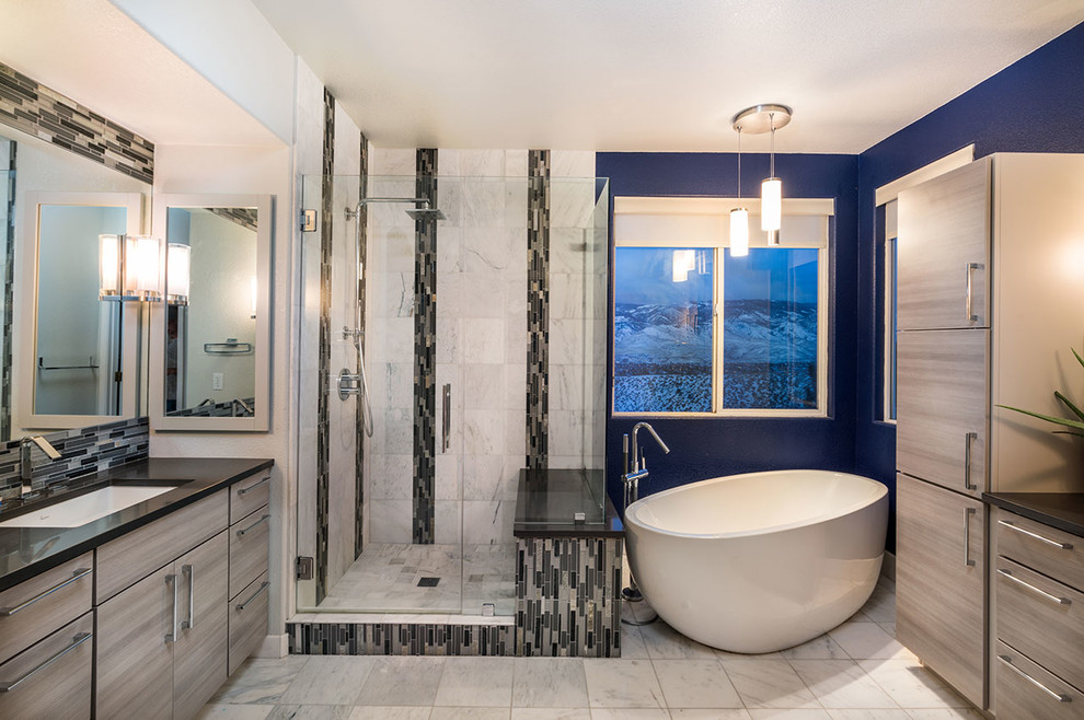 Example of a trendy master beige tile and porcelain tile porcelain tile and beige floor freestanding bathtub design with flat-panel cabinets, brown cabinets, blue walls, an undermount sink and a hinged shower door