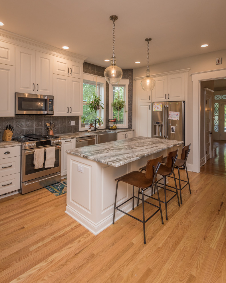 Design ideas for a traditional l-shaped kitchen in Louisville with a farmhouse sink, raised-panel cabinets, white cabinets, grey splashback, stainless steel appliances, medium hardwood floors, with island, brown floor and grey benchtop.