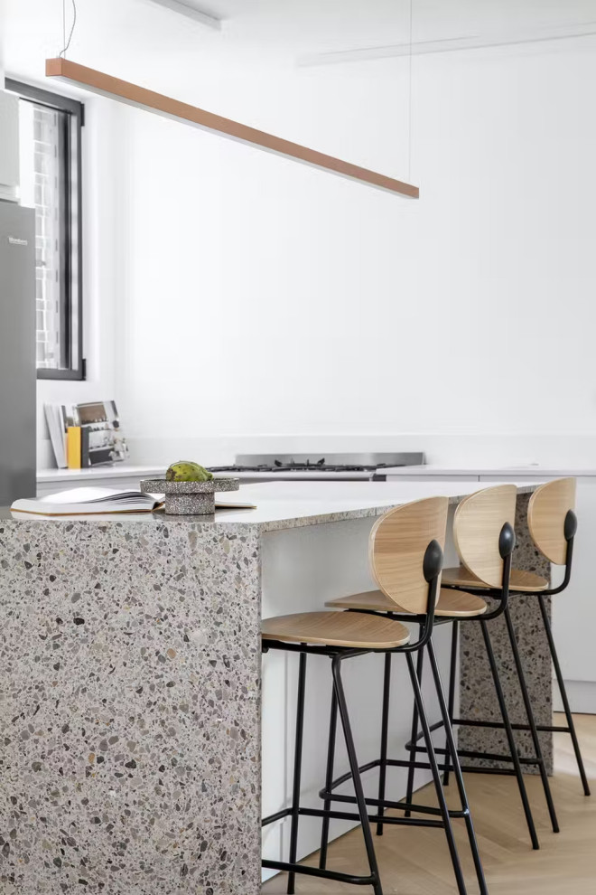 Inredning av ett mellanstort grå grått kök, med släta luckor, vita skåp, bänkskiva i terrazo, vitt stänkskydd, rostfria vitvaror, plywoodgolv, en köksö och beiget golv